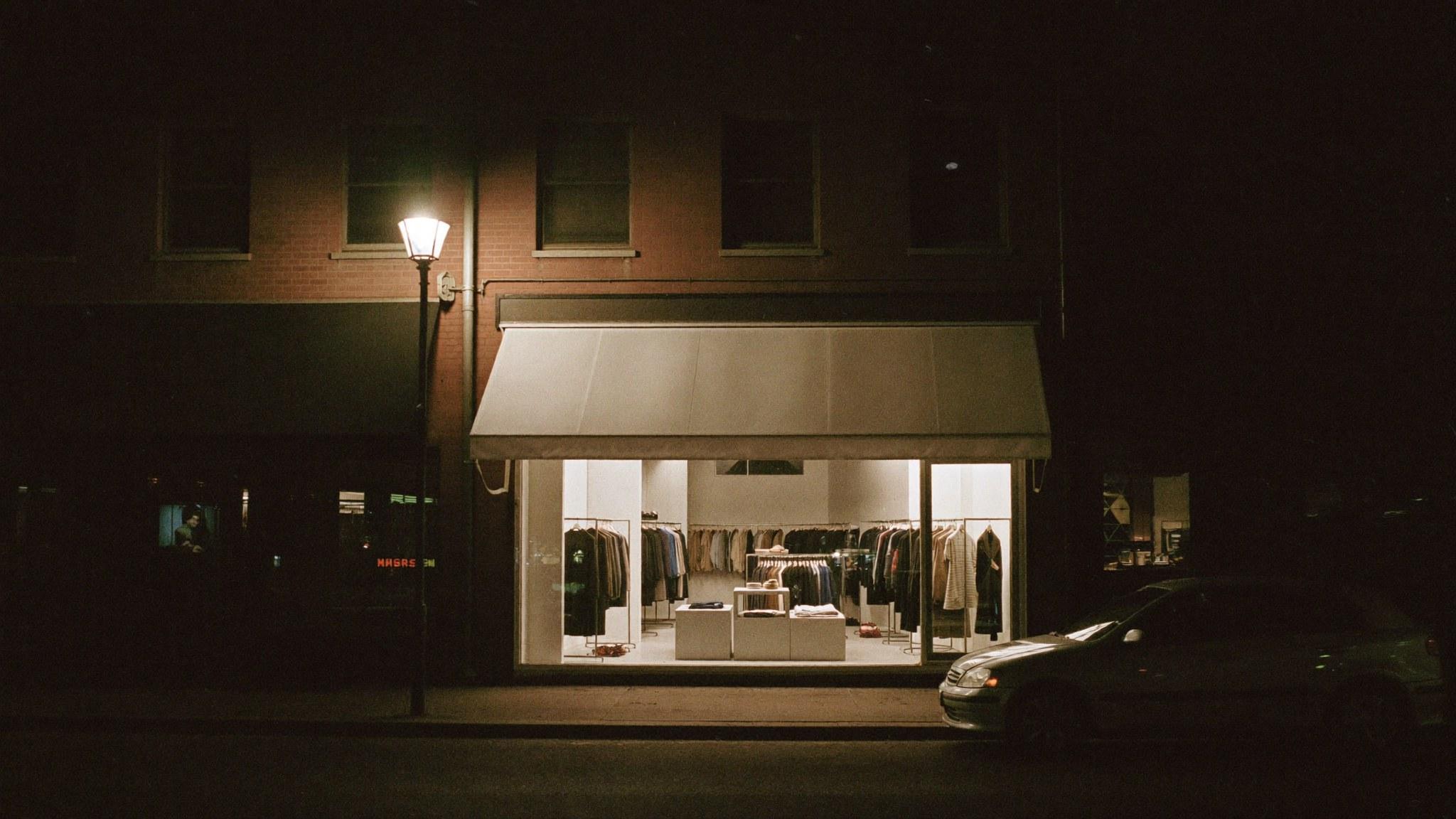 A lit boutique at night on a small-town main street, seen from across the road.